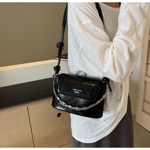 Detail of black glossy leather bucket bag with silver chain and knotted strap on model