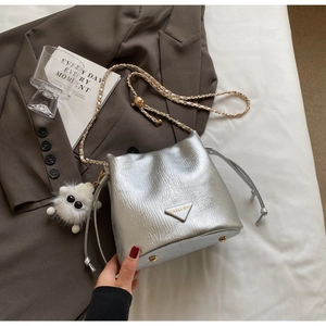 Close-up of silver bucket bag with chain strap, logo plaque and plush charm detail
