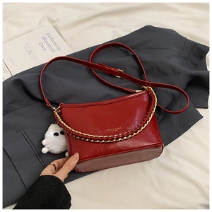 Macro view of red glossy leather bag featuring golden chain handle and white plush charm