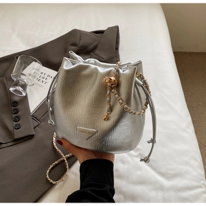 Close-up of silver pleated bucket bag with metallic texture and woven chain strap