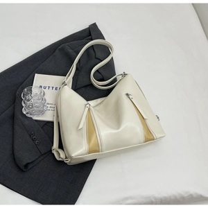 Detail of cream faux leather tote bag with decorative zippers on a minimalist backdrop