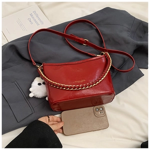 Detailed view of shiny red leather handbag with gold chain handle and plush ball charm