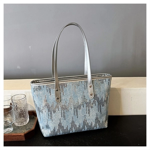 Detail of light blue tote bag featuring silver wave patterns and long metal handles