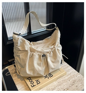 Detail of beige pleated nylon crossbody bag with adjustable strap on marble surface