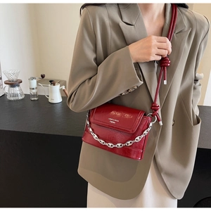 Detail of burgundy glossy leather bucket bag with silver chain and knotted shoulder strap
