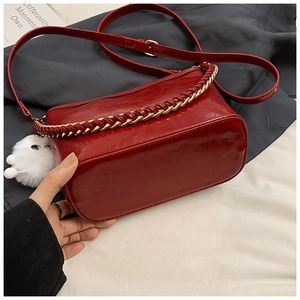 Detail of burgundy bucket bag with woven chain strap and white pompom accessory