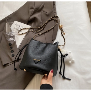 Detail of black pebbled leather bucket bag with gold chain strap and plush keychain