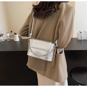 Detail of silver metallic crossbody bag with chunky chain and knot strap on a model