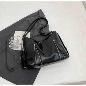 Detail of black glossy faux leather bag featuring three silver zippers and modern punk style
