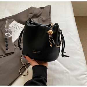 Close-up of black lychee leather bucket bag featuring gold chain and triangle logo