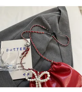 Détail d'un sac seau rouge avec nœud en perles et bandoulière sur un blazer gris
