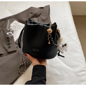 Detail of black pebbled leather bucket bag with gold chain and white plush charm