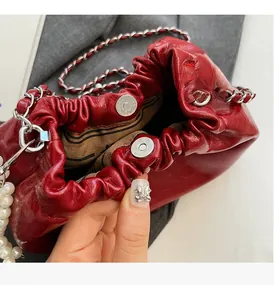 Détail du sac plissé rouge avec finition brillante, chaîne argentée et accents de perles