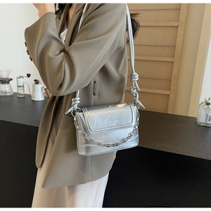 Detail of silver bucket bag with knotted shoulder strap and sleek metal chain accent
