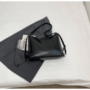 Detailed view of high-gloss black patent leather tote bag on a grey fabric background