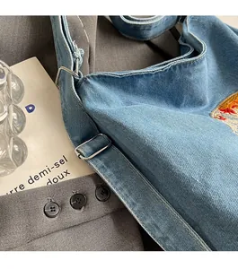 Detail of blue denim backpack showing silver metal buckle and colorful embroidery pattern