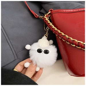Close-up of a white plush keychain with a knitted hat and sunglasses on a red handbag