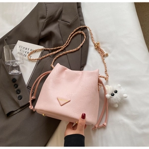Pink drawstring bucket bag with embossed texture, gold chain strap, and plush charm