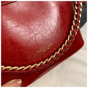 Detail of burgundy wax leather texture and gold chain strap on a chic shoulder bag