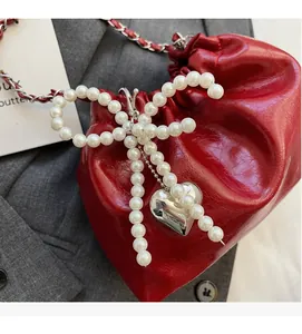 Détail du sac seau rouge avec nœud en perles et pendentif cœur argenté élégant