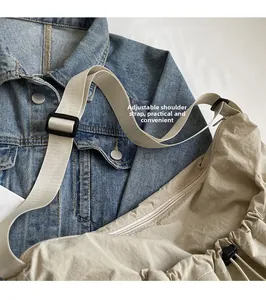 Detail of adjustable woven shoulder strap with plastic buckle on khaki pleated crossbody bag