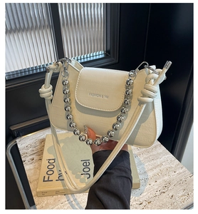 Close-up of beige crocodile texture handbag with silver bead chain and fashion logo