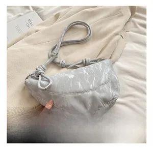 Detail of grey crescent bag showing glossy wrinkled texture and knotted rope shoulder strap