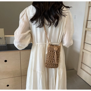 Detail of woven straw crossbody bag featuring side tassels and intricate mesh texture