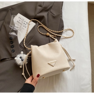 Detail of cream bucket bag with litchi texture, chain strap, and golden adjustable buckle
