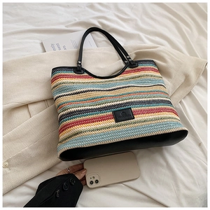 Close-up of rainbow striped woven tote bag with black leather handles and logo patch