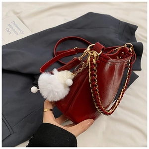 Detail of a dark red glossy leather shoulder bag with gold chain and plush charm