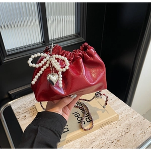 Détail du sac seau en cuir verni rouge avec nœud en perles et bandoulière en chaîne