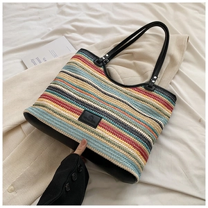 Detail of multi-colored striped woven tote bag with black leather handle and logo patch