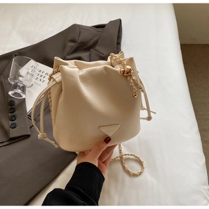 Detail of cream bucket bag with textured leather, drawstring closure and golden chain strap