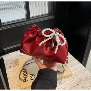 Détail du sac seau rouge brillant avec pendentif nœud perlé et bandoulière chaîne