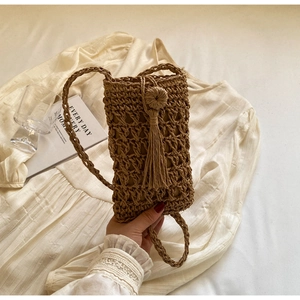 Detail of woven straw phone bag featuring a decorative ball clasp and tassel trim
