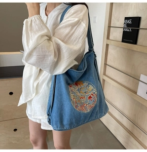 Detail of blue denim hobo bag featuring intricate colorful dragon embroidery and wide strap