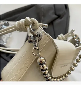Detail of a creamy white glossy leather bag with oversized silver bead chain strap