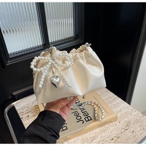 Détail du sac seau crème avec nœud en perles, breloque cœur argentée et bandoulière