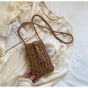 Detail of hand-woven straw crossbody bag with tassels and bohemian hollow knit pattern