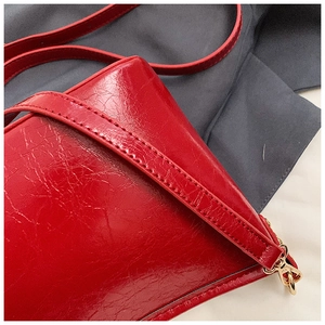 Detail of red glossy wrinkled leather shoulder bag with fine stitching and gold hardware
