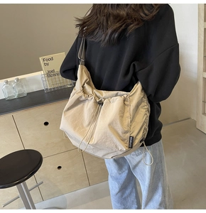 Detail of beige nylon drawstring crossbody bag with pleated sides and brand tag