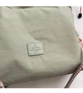Detail of light green waterproof nylon bag featuring premium leather label and woven drawstring