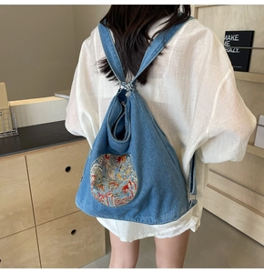 Detail of blue denim backpack showing intricate traditional circular embroidery and metal buckle