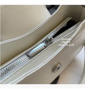 Close-up of smooth silver metal zipper and magnetic buckle on cream leather crossbody bag