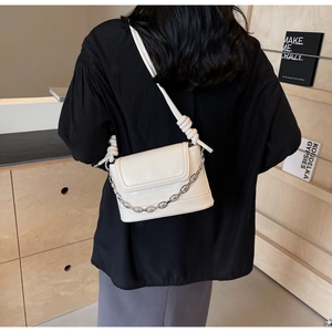 Detail of ivory bucket bag featuring silver chain and knotted strap on female model