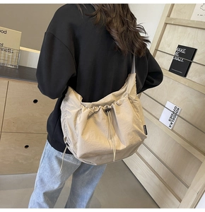 Detailed view of a beige nylon tote bag showing the side drawstring and logo tag detail