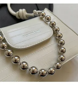 Close-up of white embossed leather bag with silver bead handle and metal lettering