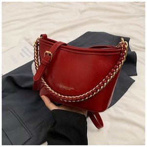 Detail of red patent leather shoulder bag with gold chunky chain strap on grey suit