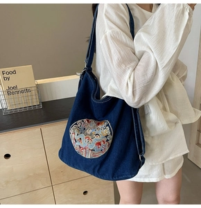 Detail of dragon embroidery on a dark blue denim crossbody bag with metal ring hardware